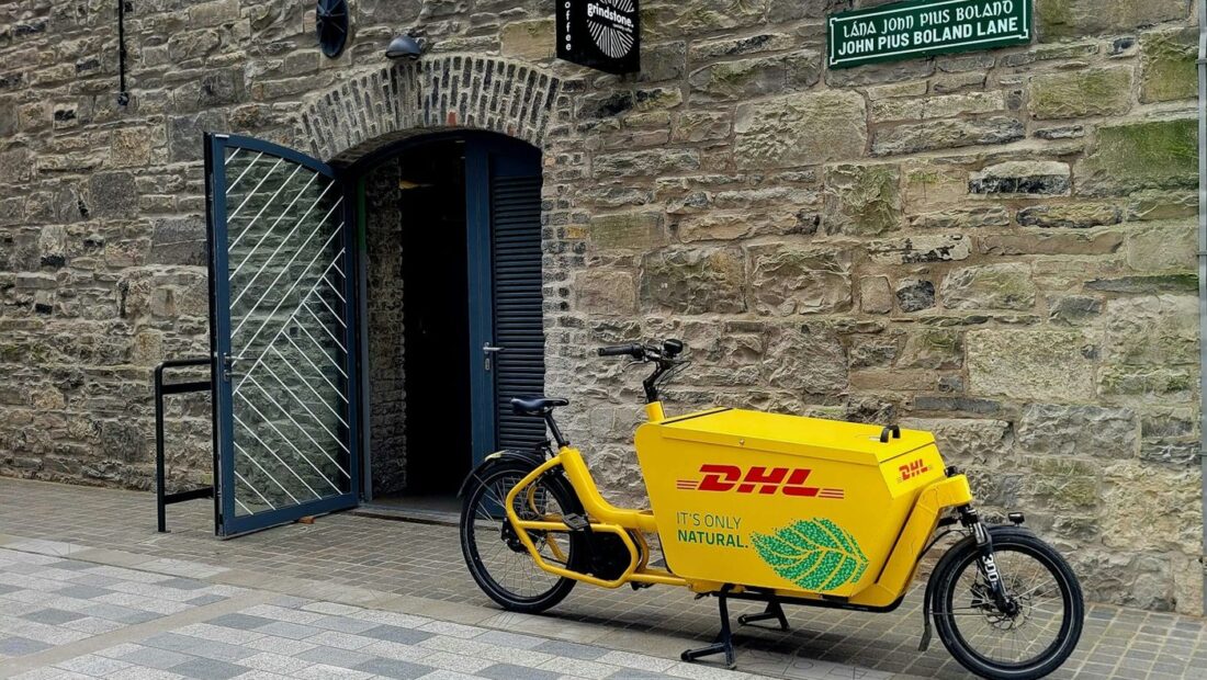 Vélo cargo de livraison jaune marqué au nom de son exploitant, garé dans une rue pavée