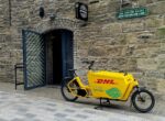 Vélo cargo de livraison jaune marqué au nom de son exploitant, garé dans une rue pavée