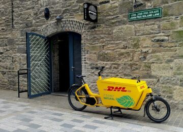 Vélo cargo de livraison jaune marqué au nom de son exploitant, garé dans une rue pavée
