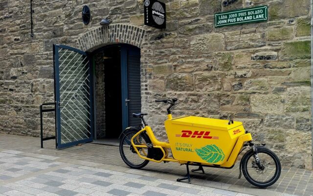 Vélo cargo de livraison jaune marqué au nom de son exploitant, garé dans une rue pavée